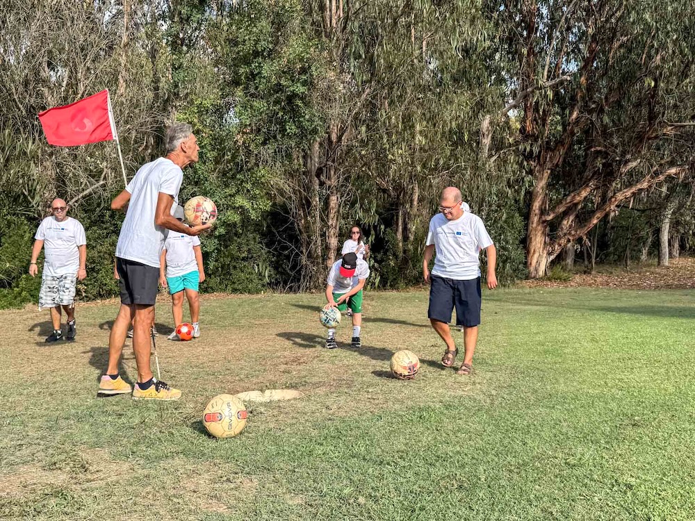 Partecipanti al Progetto Icaro provano il footgolf intorno alla buca con bandierina rossa all’Acquabona, Marelba 2026