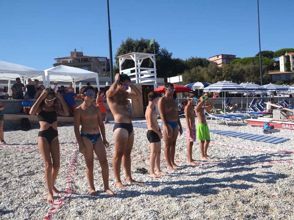 Partecipanti in costume e cuffia schierati sulla spiaggia lungo le corsie prima della prova di nuoto del Progetto Icaro, Marelba 2026