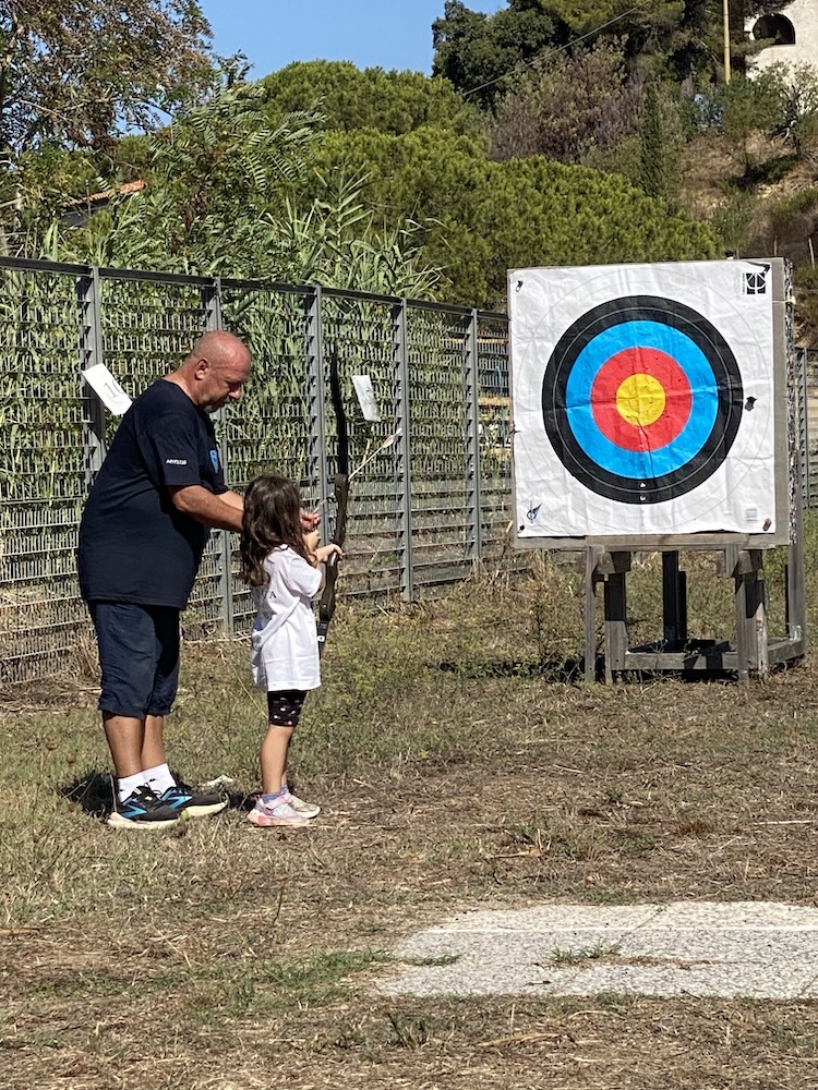 Un adulto assiste una bambina davanti al bersaglio durante l’attività di tiro con l’arco di Marelba 2026