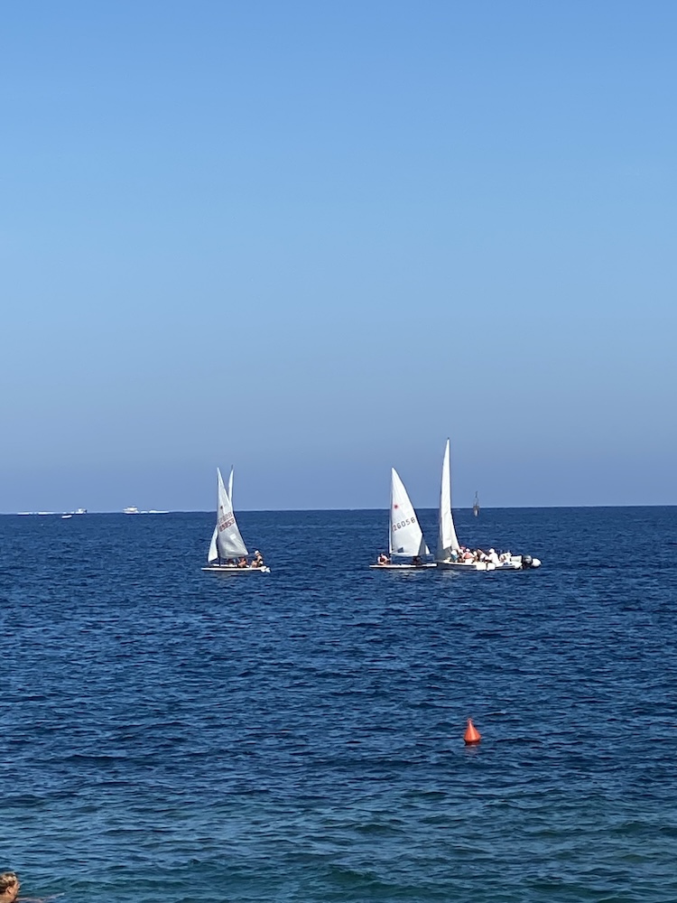 Piccole barche a vela con vele bianche navigano al largo durante le attività di vela di Marelba 2026