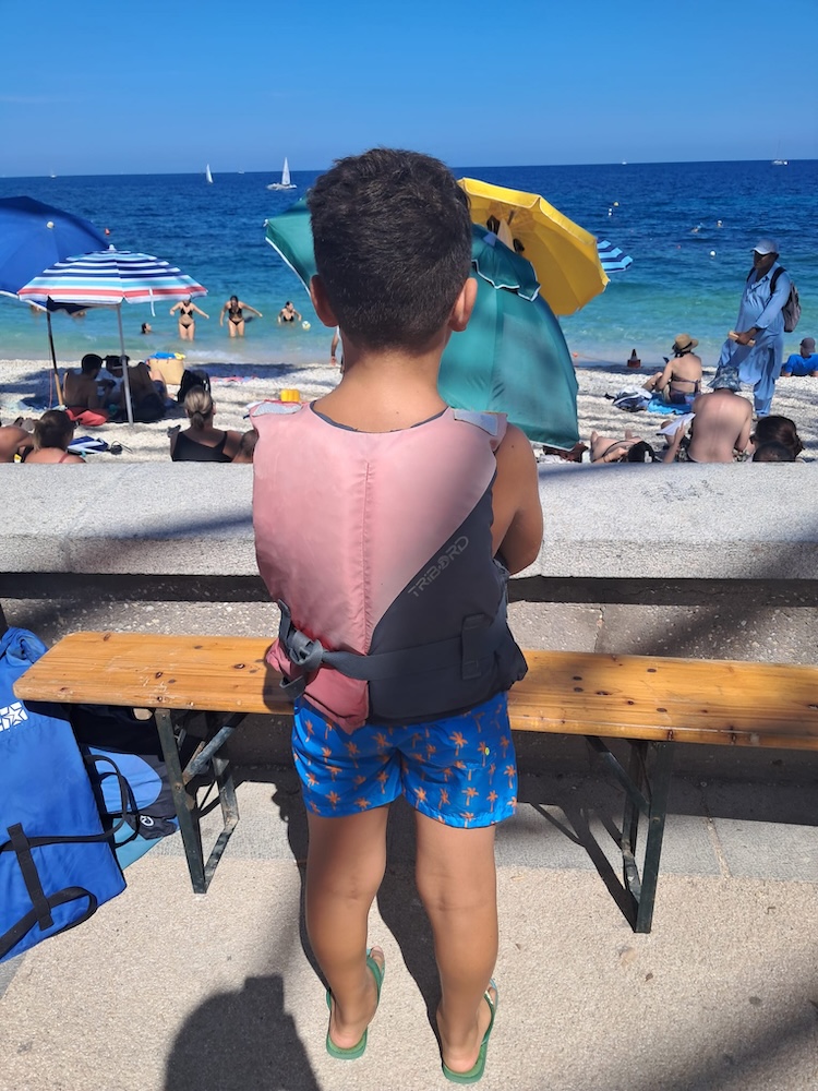 Un bambino di spalle indossa il giubbotto salvagente sulla spiaggia prima dell’uscita in mare, Marelba 2026