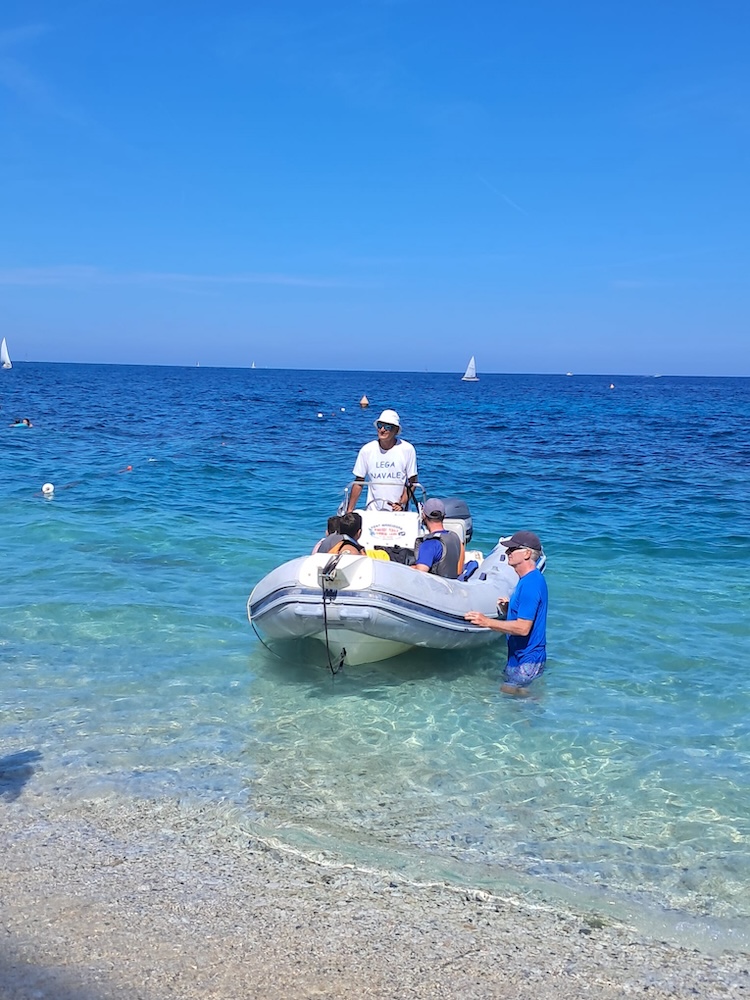 Un gommone visto di prua nelle acque basse, con i partecipanti a bordo e un accompagnatore accanto, Marelba 2026